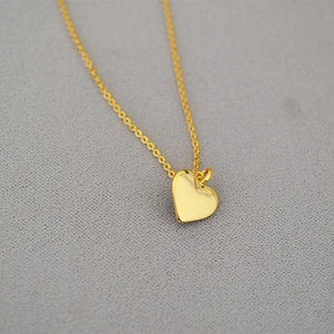 Polished gold heart pendant necklace with fine chain on textured fabric background