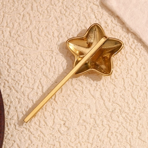Polished 18K gold plated stainless steel star hair clip on beige textured fabric background