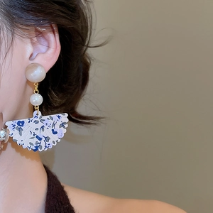 Close-up of fan-shaped resin drop earring with floral pattern and pearl details