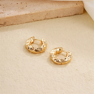 Detailed view of golden irregular hammered texture hoop earrings on a stone surface