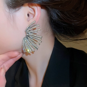 Close-up of fan-shaped silver stud earrings with crystals worn by a model in soft light