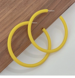Macro detail of yellow matte acrylic hoop earrings on a dark wood texture background