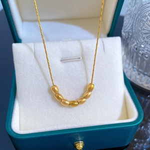 Detail of golden bead pendant necklace on white lining inside a green jewelry box