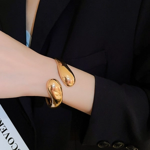Dettaglio del bracciale aperto dorato largo minimalista con finitura lucida a specchio