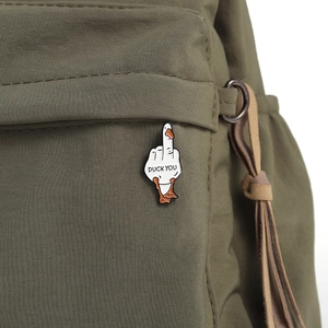 Close-up of funny white duck enamel pin with 'DUCK YOU' text on a green backpack