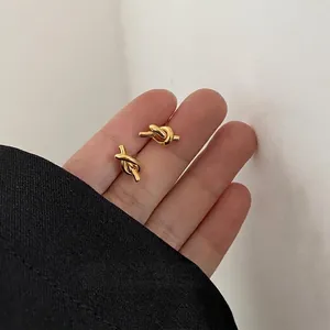 Minimalist gold knot stud earrings for women and men shown in hand for scale