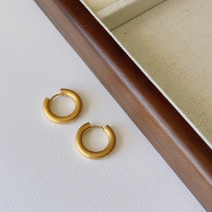 Macro shot of matte gold hoop earrings with brushed metal texture and a wooden jewelry box