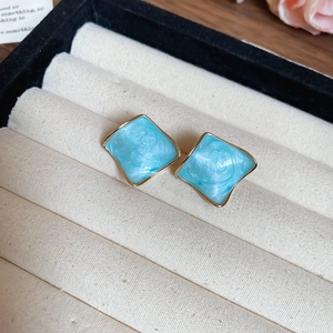 Macro shot of light blue resin earrings with gold edges on beige velvet padding