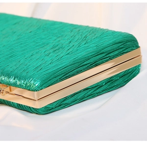 Close-up of emerald green pleated fabric evening bag with polished gold metal frame