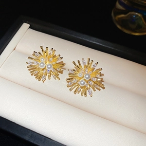 Detailed view of golden firework stud earrings with zircon crystals and faux pearls