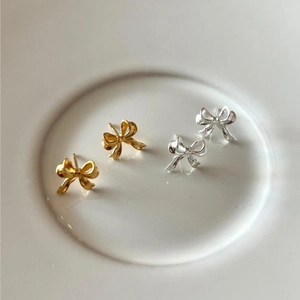 Close-up of elegant gold and silver bow stud earrings on a white ceramic tray