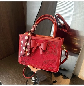 Detail of red bridal handbag with lace embroidery, large bow and heart print silk scarf