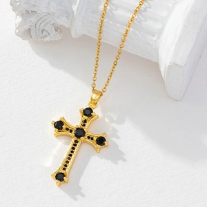 Gold cross necklace with black cubic zirconia on a white column stand