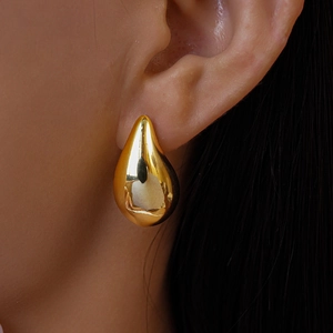 Close-up of polished gold-tone teardrop earring worn by a model in a minimalist style