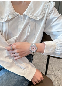 Detail of silver ladies quartz watch with pink rhinestone dial worn with a ring