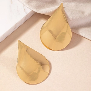 Detailed macro view of gold water drop earrings with a polished mirror finish on marble