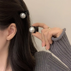 Detailed view of small black hair clip featuring a large glossy white pearl on gray fabric