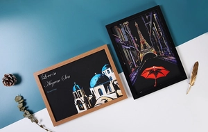 Framed scratch art showing Santorini and Eiffel Tower in wood and black frames