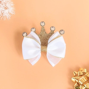 Close-up of a white satin bow hair clip with gold glitter crown and rhinestone detail