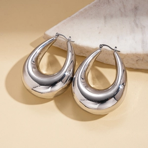 Close-up of silver hollow teardrop earrings on beige texture and white stone