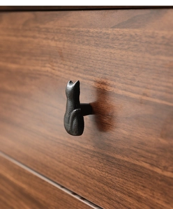 Detail of a matte black cat-shaped cast iron handle mounted on a dark wood drawer