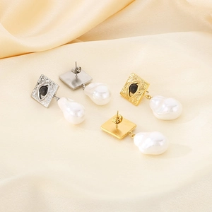 Detail of square steel earrings with evil eye center and baroque pearl pendant