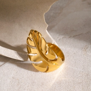 Detailed macro view of gold monstera leaf ring resting on a beige stone texture