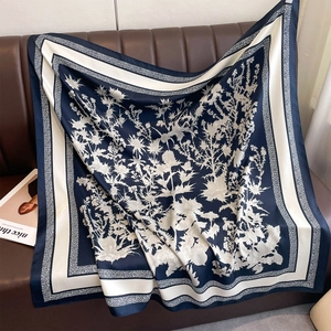 Detail of floral printed navy silk square scarf draped on a leather sofa surface