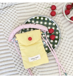 Detail of yellow fabric phone bag featuring pink padded handle with text and red button