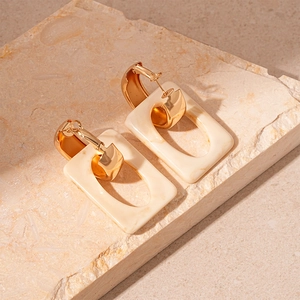 Detail of geometric rectangular earrings in gold metal and cream resin on stone base