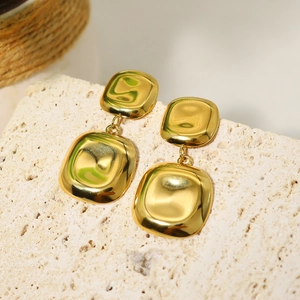 Macro detail of gold geometric square drop earrings on a natural stone background