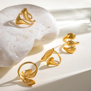 Polished gold irregular water drop open rings displayed on textured white stone
