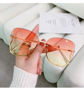 Detail of rimless butterfly sunglasses with orange gradient lenses and gold metal temples