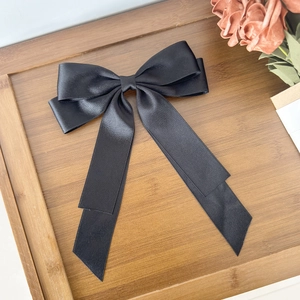 Elegant large black satin bow hair clip on wooden tray with orange rose decoration