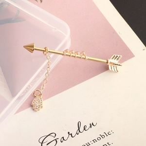 Detail of a golden arrow industrial bar with chain and rhinestone palm charm pendant
