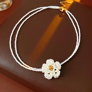 Detail of double-layer white seed bead necklace with a floral camellia pendant