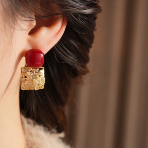 Macro view of model wearing a red square zircon earring with gold frame detailing