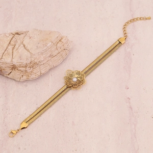 Detail of gold flower bracelet with pearl center on layered snake chain over stone