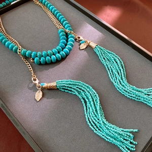 Detail view of turquoise beaded tassel necklace with golden leaf charms on a dark tray