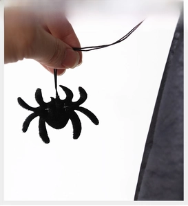 Detail of a small black plush spider charm with a thin lanyard for Halloween hats