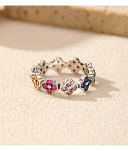 Macro shot of silver clover ring with multi-colored gemstones on a textured sandy surface