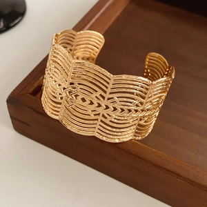 Détail d'un bracelet manchette doré large avec des motifs ajourés en dentelle fine