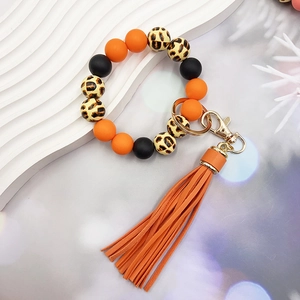 Dettaglio di perline in silicone arancione e leopardate con nappa in pelle e gancio oro