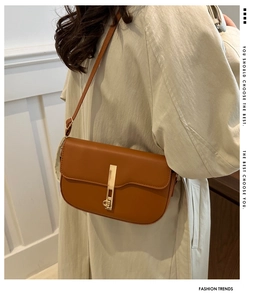 Detail of trendy caramel leather saddle bag featuring a stylish golden rectangular metal buckle