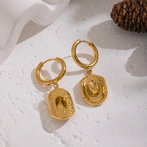 Golden hoop earrings with cowboy hat charms on a white textured surface with pine cone