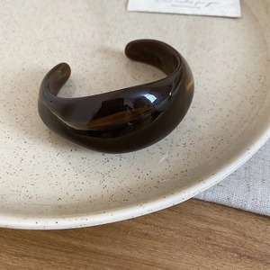 Close-up of a wide amber acrylic resin open cuff bracelet on a vintage ceramic plate