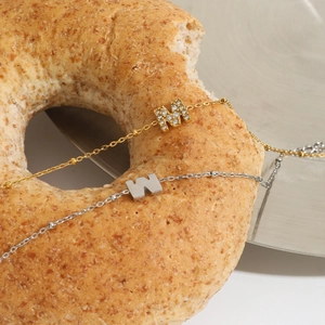 Detail of gold and silver chain bracelets with M and W pendants on a creative prop