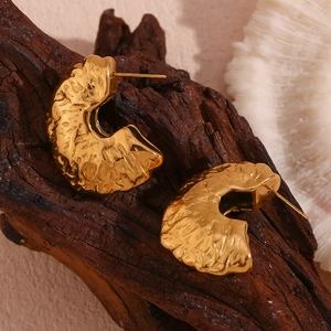 Detailed close-up of 18K gold plated fan earrings with hammered texture on dark wood