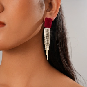 Détail de la boucle d'oreille en velours rouge avec franges en strass dorés sur modèle