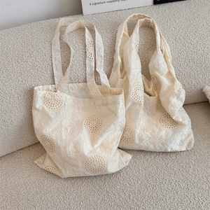 Close-up of two cream canvas tote bags with hollow floral embroidery on a soft sofa